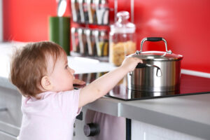 Kind steht in der Küche und greift zum Kochtopf mit kochendem Wasser.