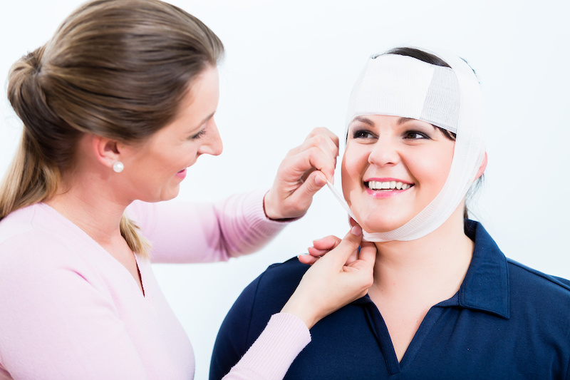 Im Erste Hilfe Kurs für betriebliche Ersthelfer üben 2 Frauen den Kopfverband. Die verletzte Frau freut sich über die gute Hilfe.