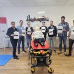 7 Personen halten ihre Teilnahmebscheinigung über den bestanden ACLS Refresher Kurs hoch. Im Vordergrund eine Simulationspuppe auf einer Rettungstrage.