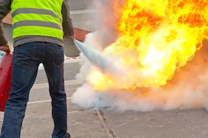 Ein Brandschutzhelfer löscht mit einem Feuerlöscher einen Brand im Brandschutzhelfer / Evakuierungshelfer Kurs in Bonn. Er trägt eine gelbe Warnweste.